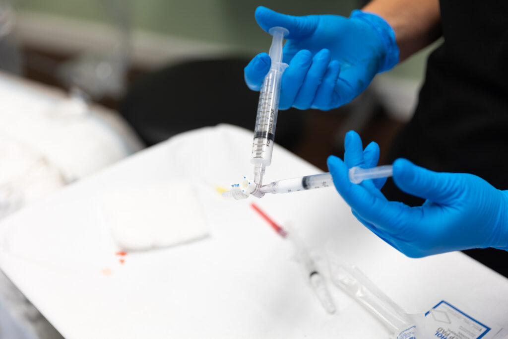 A close-up of a specialist in blue gloves preparing injectable foam syringes for a vein treatment in Wellen Park.