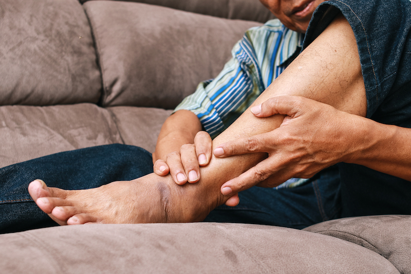 Man on couch cradling his leg/ankle because of aching leg pain before going to see a vein clinic near me in Englewood, FL